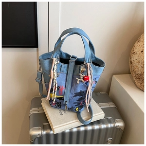 Close-up of denim bucket bag with graffiti prints, charms and silver balloon dog on books