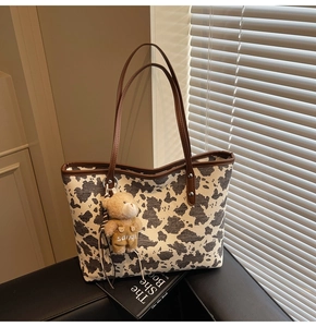 Detail of cow print canvas tote bag with leather straps and a small plush bear charm