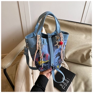 Detail of light blue denim bucket bag featuring red Smiley graffiti and colorful charms