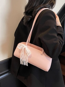 Pink baguette bag with white lace bows worn by a model in a black blazer