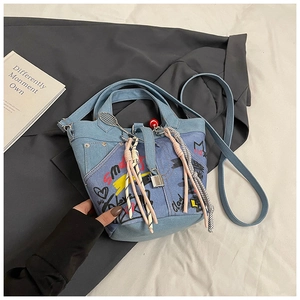 Close-up of patchwork denim bucket bag with graffiti prints and tassels