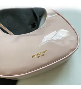 Detail of glossy pink patent leather saddle bag with gold logo and smooth curves