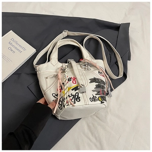 Close-up of white bucket bag with street graffiti prints and woven rope pendant detail