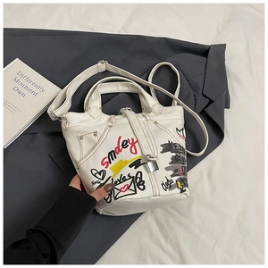 Detail of white canvas bucket bag featuring street style graffiti and metal lock detail