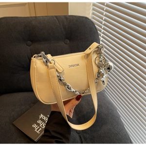 Détail du sac baguette beige avec chaîne dorée et breloque de dessin animé sur velours côtelé