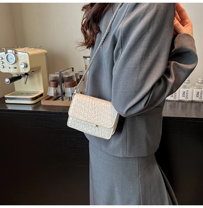 Detailed macro view of cream crossbody bag featuring woven texture and silver chain strap