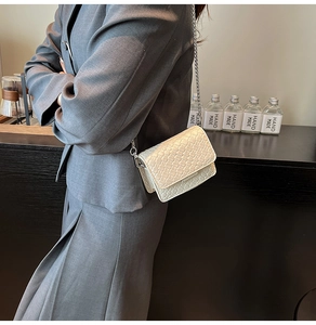Detail of cream woven mini crossbody bag with delicate silver chain strap on model
