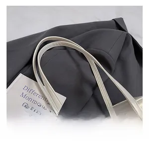 Detailed close-up of glossy white tote bag handles on a grey suit and art book
