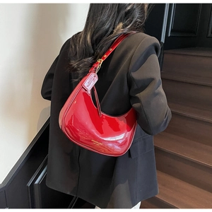 Détail du sac demi-lune en cuir verni rouge avec bandoulière sur un blazer noir