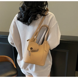 Back view of model wearing beige litchi grain leather bucket bag with adjustable strap