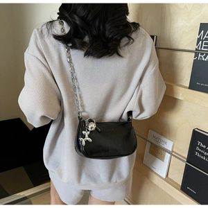Détail du sac demi-lune noir avec chaîne argentée et breloque chien ballon sur haut gris gaufré