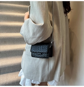 Detail of black woven crossbody bag with silver chain strap shown on model's side