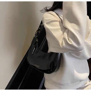 Detail of high-gloss black patent leather hobo bag with gold logo and chain strap