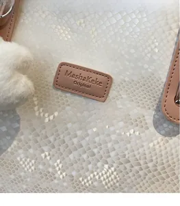 Close-up of snakeskin textured tote bag with brand logo tag and fluffy white pompom charm