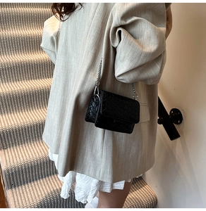 Detail of black woven mini crossbody bag with a sleek silver chain strap on a model