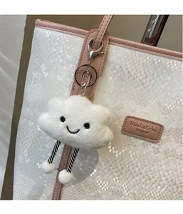 Cute white plush cloud keychain with smile face on a stylish snakeskin tote bag