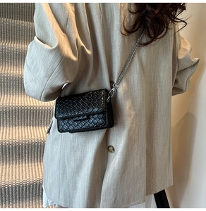 Detail of black woven leather mini crossbody bag with silver chain strap on model
