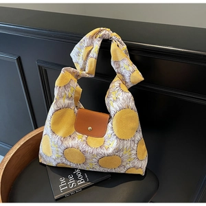 Detail van canvas draagtas met zonnebloemprint, bruine lederen flap en gouden metalen knop