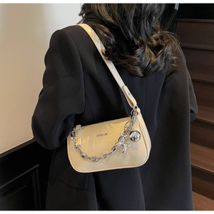 Détail du sac bandoulière en cuir beige avec chaîne argentée et breloque chien ballon
