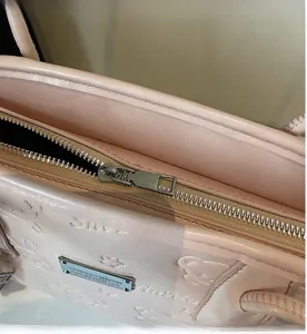 Detail view of pink shoulder bag showing smooth zipper closure and metallic brand plate
