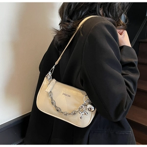 Détail du sac à bandoulière en cuir verni beige avec chaîne argentée et breloque