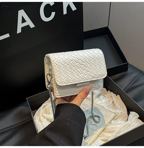 Detail of white woven leather mini bag with silver chain strap on gift box background