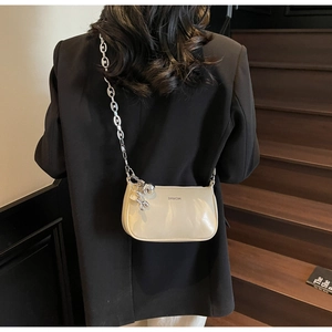 Détail du sac bandoulière beige brillant avec chaîne argentée et pendentif ours