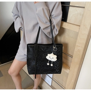 Detail of black snake-embossed tote bag featuring a white cloud plush charm and long straps