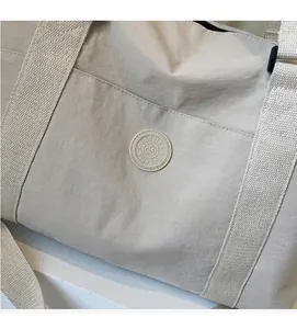 Detalle del bolso de viaje beige con tela de textura suave y logotipo de moda