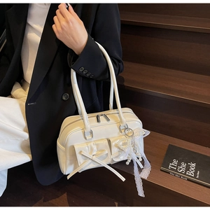 Detail of cream patent leather bowling bag with bow pocket and pearl lace charm