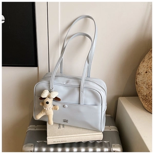 Close-up of light blue tote bag with plush dog charm and metal logo on silver suitcase