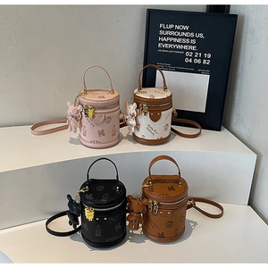 Detailed view of four colorful cylindrical leather bags with teddy bear print on white stand