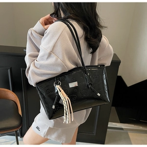 Detail of glossy black patent leather tote with embossed cartoon bears and woven tassel charm