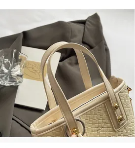 Detail of cream woven bucket bag with gold studs and brand logo on grey suit