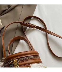 Detail of adjustable leather strap, zipper closure and golden bear pendant on barrel bag