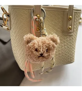 Detail view of a fluffy light brown bear charm with braided lanyard on a woven handbag