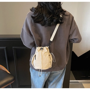 Detail der beigen Kordelzug-Beuteltasche mit langem Gurt und seitlicher Netztasche am Modell