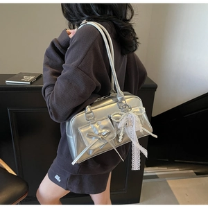 Detail of silver shoulder bag featuring a lace bow, pearl charm, and metallic finish