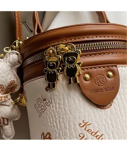 Detail of bear-shaped gold zippers and brown leather texture on a cylinder bag