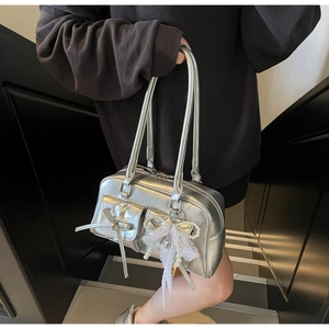 Detail of silver metallic bowling bag featuring flap pockets and lace pearl charm