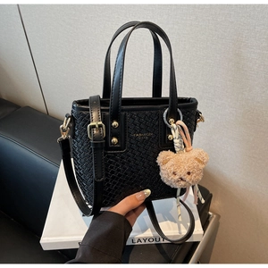 Close-up of black woven bucket bag with golden logo plaque and a cute brown plush bear charm