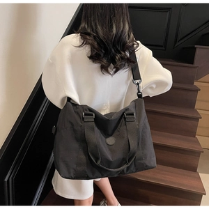 Detailed view of the large black travel tote bag worn across the shoulder by a model