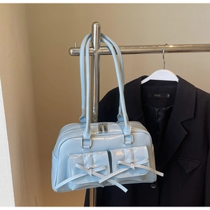 Close-up of light blue glossy handbag with bow details and twin front flap pockets