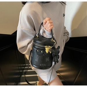 Detail of black cylindrical crossbody bag with teddy bear embossing and golden hardware