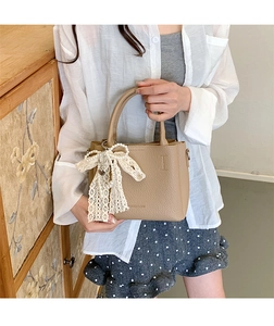Dettaglio borsa beige in pelle martellata con fiocco in pizzo bianco e ciondolo di perle