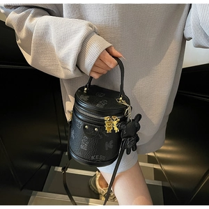 Detail of a black leather cylinder bag with bear charms and metal K logo on a staircase