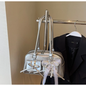 Silver metallic handbag featuring lace bow charm and front pocket detail on beige wall