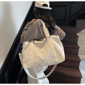 Rear view of large beige nylon travel tote bag on stairs with adjustable shoulder strap
