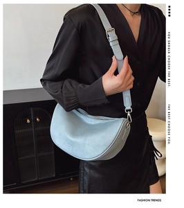 Detail of light blue textured leather crescent bag with adjustable strap and metal hardware