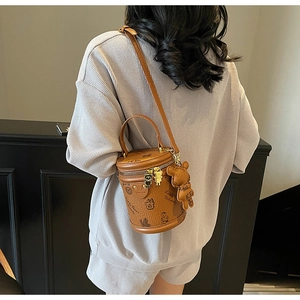 Detail of a brown cylindrical bucket bag with teddy bear prints and plush charms